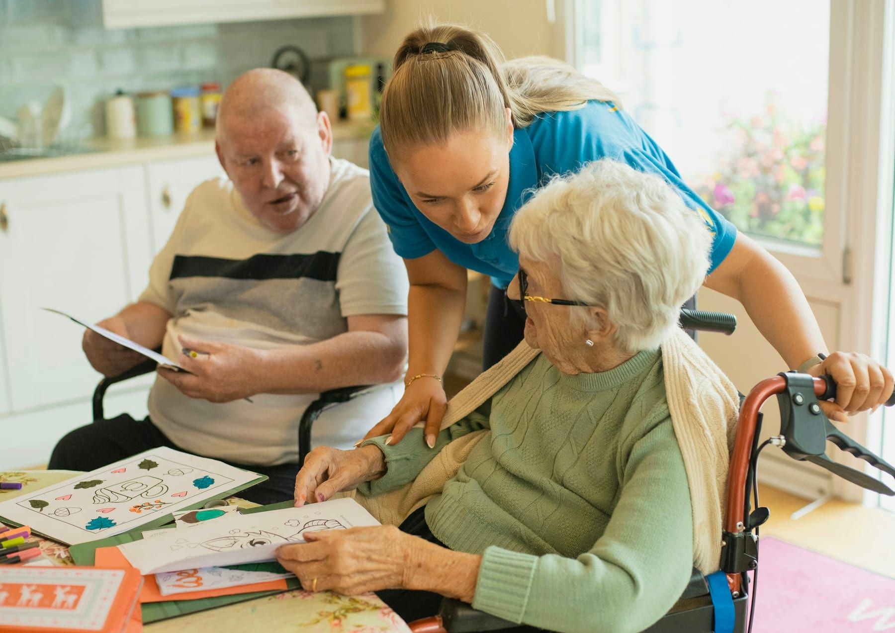 A caregiver laughs with an older couple while they color pictures at a table