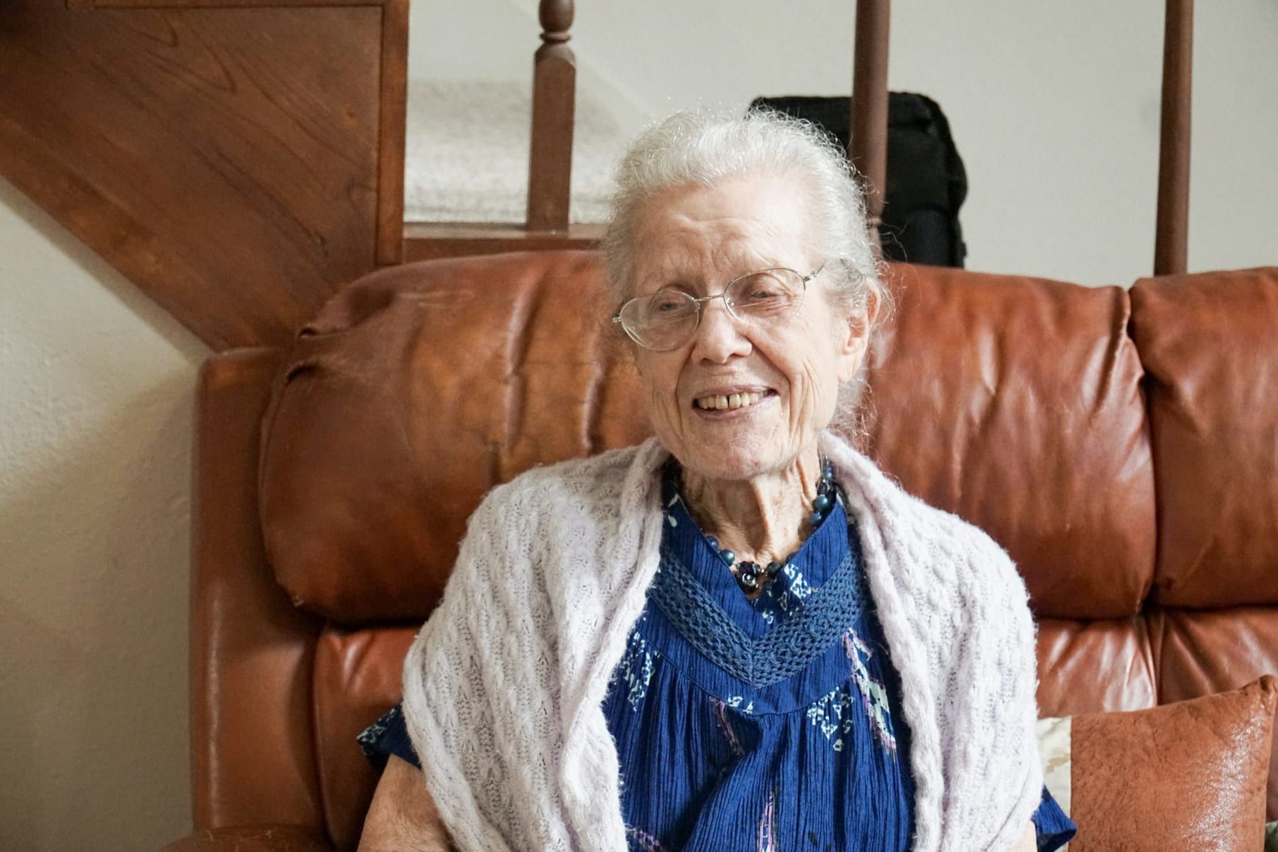 A smiling older woman sits on a leather sofa at home